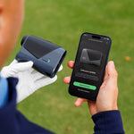 Person holding a golf rangefinder and smartphone with app on grass background