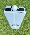 Front-facing view of the Flight Deck Putting Tour impact trainer on grass with a golf ball centred between the two black impact blocks and alignment crosshair visible