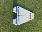 Overhead flat-lay of the Flight Deck Putting Tour Soft alignment guide on grass without a ball, showing the triangular body, blue impact blocks, and crosshair alignment lines