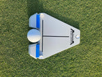 Top-down view of the Flight Deck Putting Tour Soft guide on grass with a golf ball seated between the two blue impact blocks at the ball gate