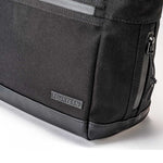 Corner detail of Fourteen Golf black cart tote bag showing ballistic nylon body, FOURTEEN rubber badge, PU leather base panel, structured bottom corner, and side zip pocket with paracord pull