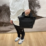Fourteen Golf black cart tote bag carried by hand by golfer in white hoodie and black pants, shown against golf course mural backdrop with water bottle visible inside