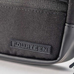 Macro detail of Fourteen Golf round pouch corner showing ballistic nylon weave texture, raised FOURTEEN rubber logo badge, and PU leather piping