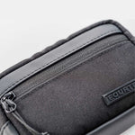 Close-up of Fourteen Golf black round pouch showing textured nylon fabric, front zip pocket, PU leather trim, and embossed FOURTEEN rubber badge