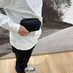 Fourteen Golf black round pouch held in hand by golfer wearing white hoodie and black pants, shown against golf course mural backdrop