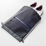 Fourteen Golf black drawstring shoe bag laid flat on white surface with pair of white golf shoes partially inserted through open top, showing front zip pocket, FOURTEEN badge, PU leather base panel, and dual drawstring closure