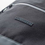 Close-up of Fourteen Golf black shoe bag front pocket showing ballistic nylon texture, zip closure with gunmetal hardware, and embossed FOURTEEN rubber badge
