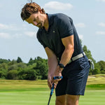 Man in black golf attire on a golf course with trees in the background