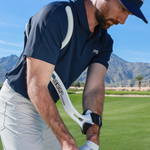 Man on a golf course with a golf club, wearing a navy blue shirt and white pants.