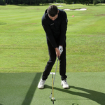 Man in black outfit practicing golf on a green course