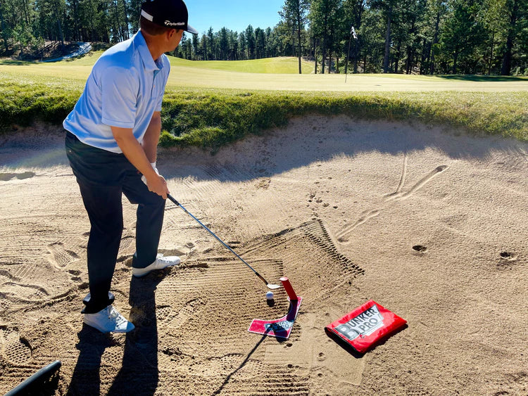 Wide-angle view of a golfer addressing the ball using the EyeLine Golf Bunker Pro System in a bunker, with the green and flagstick visible in the background
