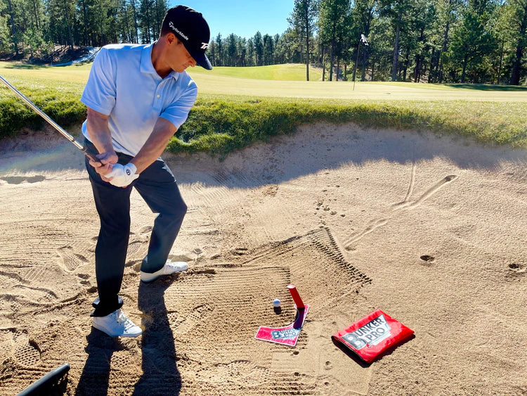 Golfer mid-downswing approaching the EyeLine Golf Bunker Pro System board and entry point peg in a course bunker during a sand shot drill
