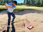 Golfer at the top of a bunker swing backswing with the EyeLine Golf Bunker Pro System entry peg and board positioned in the sand below
