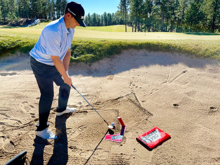 Golfer setting up address position over the EyeLine Golf Bunker Pro System board and entry peg in a course bunker, fairway and green visible in background