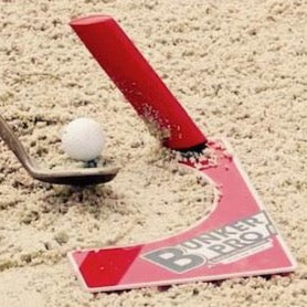 A red and white golf training aid called Eyeline Bunker Pro System, placed in a bunker with a golf ball and a club to demonstrate its use.