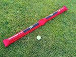 EyeLine Golf Balance Rod laid flat on grass beside a golf ball, showing the full length of the inflatable red balance training aid