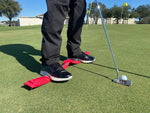Golfer putting on a practice green with the EyeLine Golf Balance Rod positioned under both feet to build a stable, repeatable putting stance