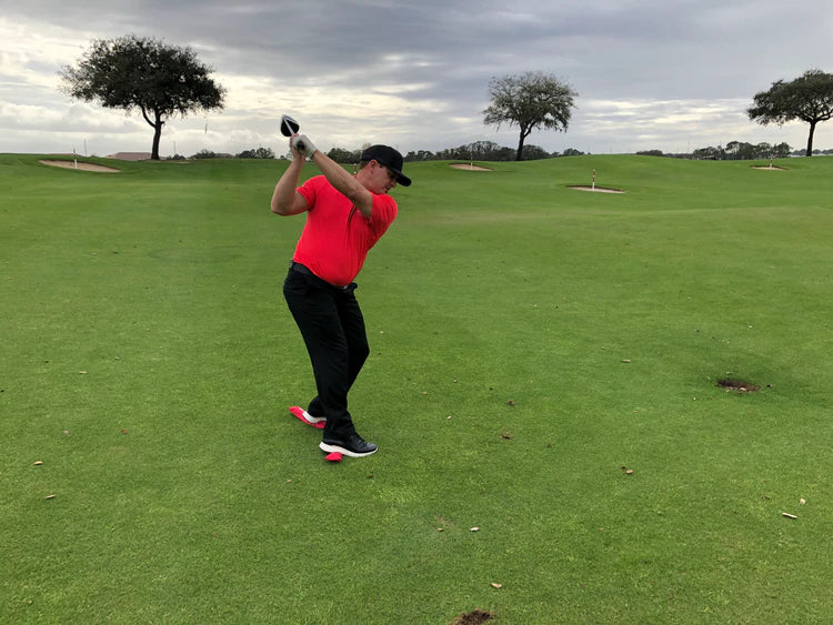 Full-swing follow-through with the EyeLine Golf Balance Rod under both feet, demonstrating improved weight transfer and balance through impact