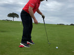 Side-on view of a golfer chipping with the EyeLine Golf Balance Rod positioned under the feet to encourage proper weight distribution at setup