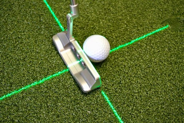 Low-angle view of putter head and golf ball positioned at the intersection of the EyeLine Golf Groove Putting Laser cross beam on a putting green