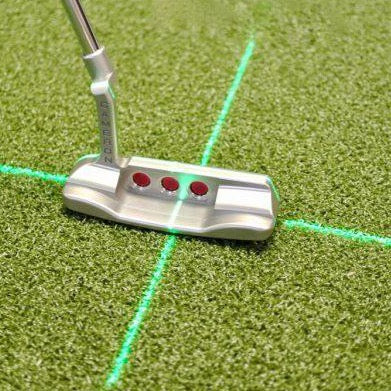 A putting laser aid with a green beam bisecting a putter head on a green surface, indicating alignment for golf putting.