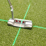A putting laser aid with a green beam bisecting a putter head on a green surface, indicating alignment for golf putting.