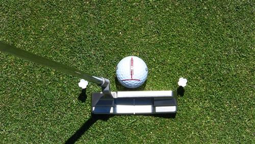 Overhead view of a putter aligned behind a golf ball marked with the EyeLine Golf Impact Ball Liner line on a putting green