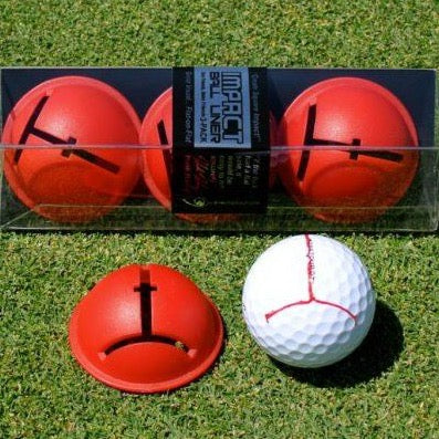 Three red golf ball impact liners with a white golf ball featuring a red line alignment aid, presented on grass.