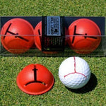 Three red golf ball impact liners with a white golf ball featuring a red line alignment aid, presented on grass.