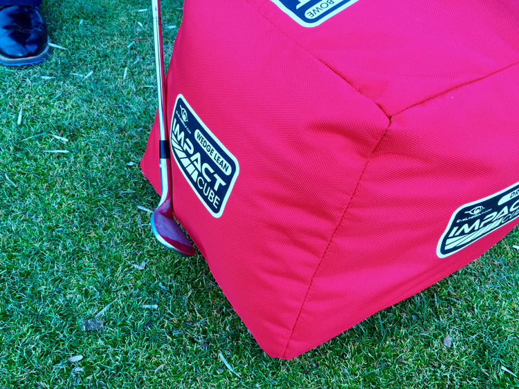 EyeLine Golf Impact Cube Wedge Lean training aid positioned against a golf club on grass, showing angled face detail