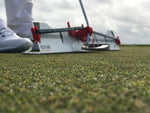 Grass-level angle of the EyeLine Golf Edge Putting Rail with Memory Band and putter at the gate, showing the low-profile rail design flush with the green surface