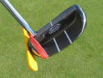 Close-up of the EyeLine Golf Putter Guide showing the yellow and red face angle indicators attached to a mallet putter head on the green