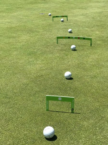 Three EyeLine Golf Putting Path Gates set up in a line on the green at increasing distances toward the hole, with golf balls placed at each gate for progressive putt accuracy drills