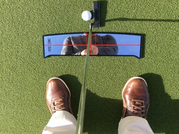 Golfer's-eye view looking down at the EyeLine Golf Shoulder Mirror reflecting upper body and shoulder alignment with red crosshair lines, putter and ball at address