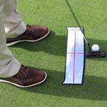 A golfer using a shoulder mirror to align with a putting green. The golfer's feet and part of his body are visible, and a golf ball and putter are also present on the green.