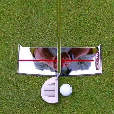 A golfer using a small, reflective putting alignment mirror on the green to align their shoulders with the mirror lines, with a golf ball and putter in the foreground.