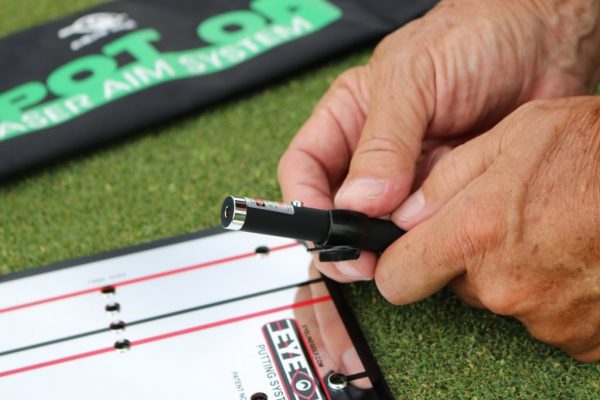 Close-up of hands attaching the EyeLine Golf Spot On Laser to a putting alignment board, with the Spot On Laser Aim System carry bag visible in the background