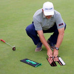 EyeLine Golf-branded instructor crouching on the green to set up the Spot On Laser alignment system beside its carry pouch and a putter