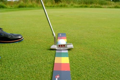 Side-angle view of putter positioned on the EyeLine Golf Stroke Meter by Todd Sones, with colour-coded backstroke and follow-through zones visible along the full length of the mat