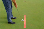 Golfer addressing a putt with a red alignment strip placed on the green to guide putter path and ball position toward the hole