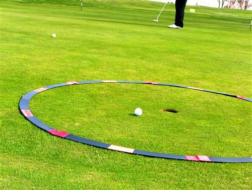 Large orange and black Eyeline Golf Target Circle laid around a flagstick on the green, with a golf ball positioned inside for proximity-to-hole putting drills