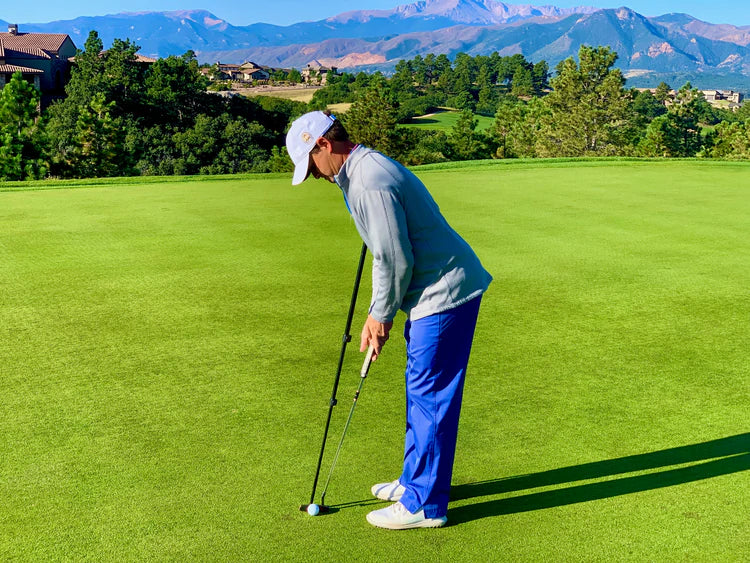 Golfer using the Eyeline Golf Putting Pendulum Rod alongside a putter at address on a scenic mountain course green