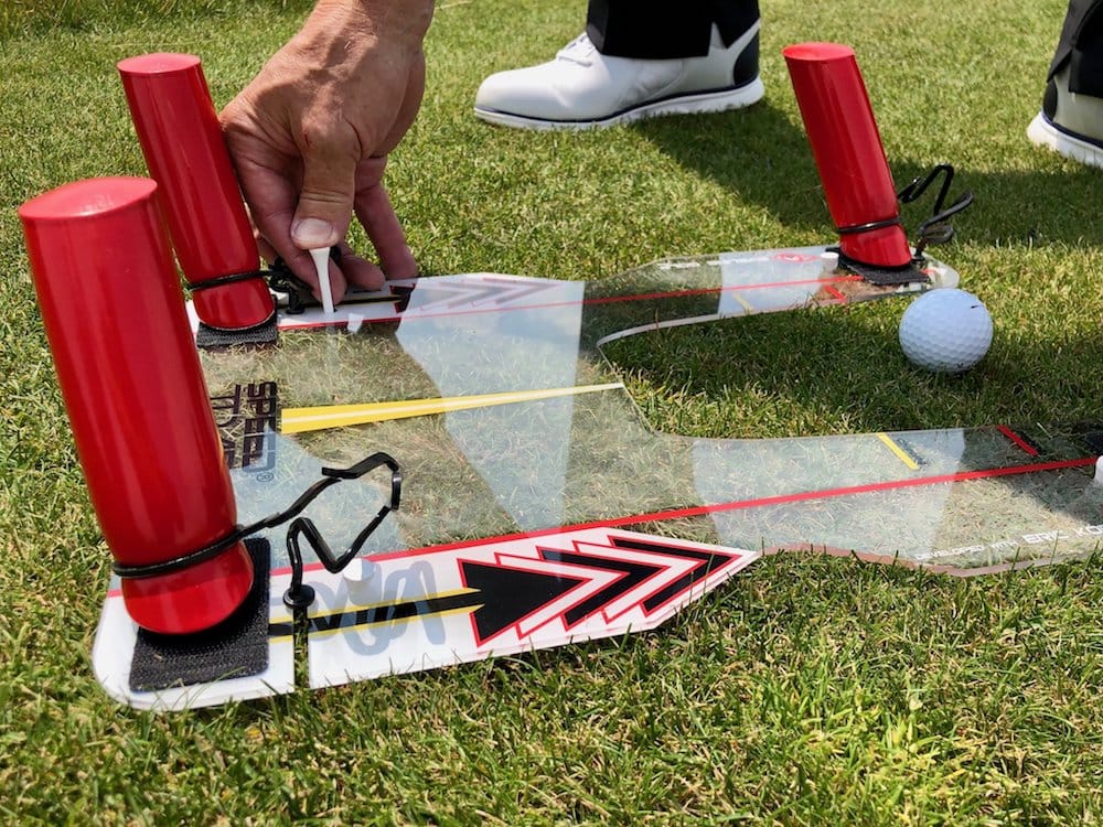 Close-up of golfer placing tee on Eyeline Speed Trap 2.0 with directional arrows and adjustable red foam barriers